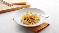 a white plate topped with pasta next to a wooden cutting board