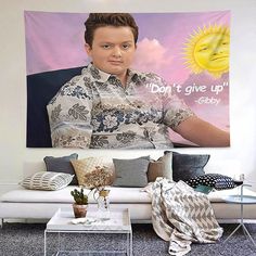 a man sitting on top of a white couch in front of a wall with a poster