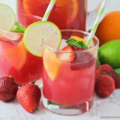 two glasses filled with watermelon and limeade next to oranges, strawberries and limes