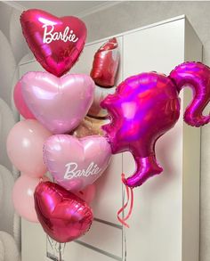 pink and red balloons with the word barbie written on them are hanging from a wall