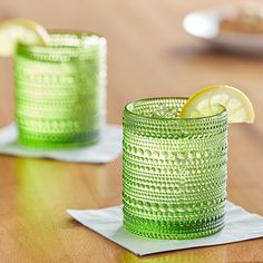 two green glasses sitting on top of a table with lemon wedges in the middle