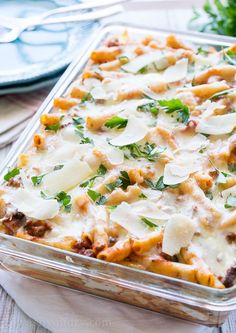 a casserole dish with meat and cheese in it on a wooden table next to silverware