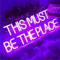 this must be the place neon sign with flowers on it and purple lighting in the background