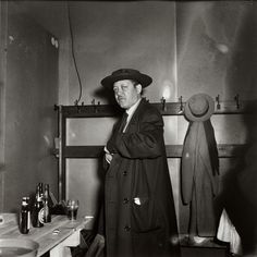 a man in a coat and hat standing next to a table