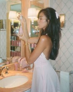 a woman in a white dress is looking at her reflection in the mirror while brushing her teeth