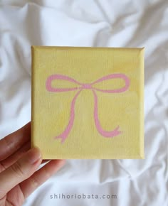 someone is holding up a small piece of paper with a pink bow on the front