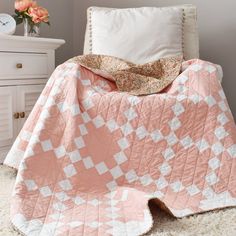 a pink and white blanket sitting on top of a bed next to a nightstand with flowers