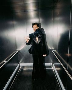 a woman standing in an elevator with her hand up to the camera and wearing a black suit