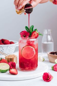 a person pouring fruit into a glass with strawberries and limes on the side