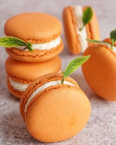 four orange macaroons with cream filling and green leafy leaves on the top