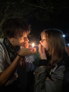 a man and woman standing next to each other with a candle in their mouth at night