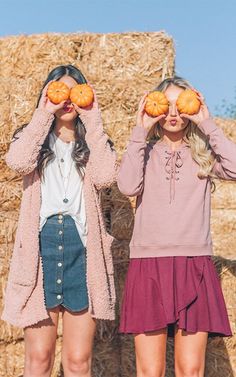 two young women standing next to each other holding pumpkins in front of their eyes