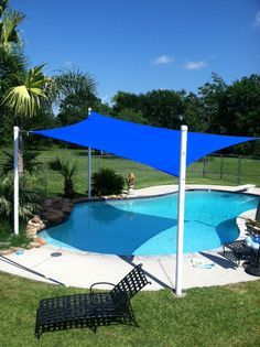 an empty swimming pool surrounded by lawn furniture and shade sailers on a sunny day