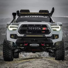 the front end of a white toyota pickup truck with its lights on, and two large tires