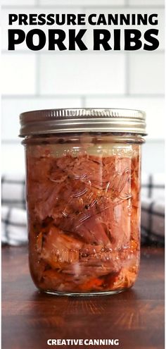 a jar filled with pork ribs sitting on top of a wooden table next to a white brick wall