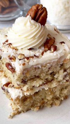 a piece of cake with white frosting and pecans on the top is sitting on a plate