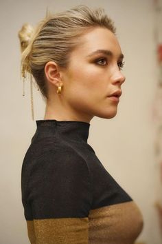 a woman with her hair in a high bun wearing gold earrings and a black top