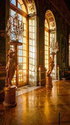 an ornate room with chandeliers and statues on the floor in front of large windows