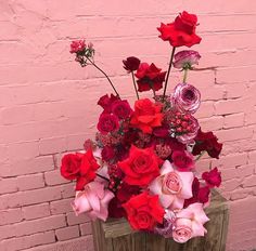 a wooden vase filled with lots of red and pink flowers next to a brick wall