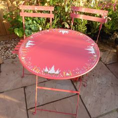 a pink table and two chairs sitting on top of a stone floor next to plants