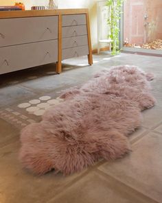 a pink sheepskin rug is on the floor in front of a dresser and mirror