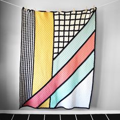 a multicolored quilt hanging on a clothes line in front of a white wall