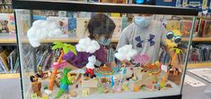 two people wearing masks behind a display case filled with toy figurines and books