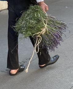 a man walking down the street carrying a bundle of grass