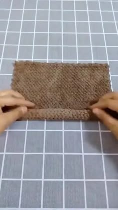 two hands that are holding a piece of cloth on a tile floor with white squares in the background