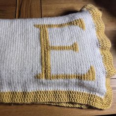 a knitted blanket with the letter f on it sitting on top of a wooden floor