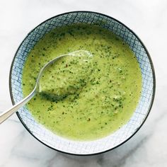 a bowl filled with broccoli soup on top of a white tablecloth next to a spoon