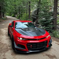 a red sports car parked on the side of a dirt road next to some trees