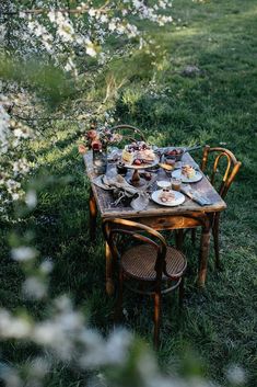 a wooden table with plates and bowls on it sitting in the middle of a field