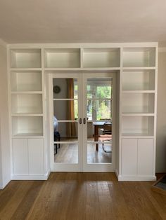 an empty living room with white bookcases and wood floors in the middle of it