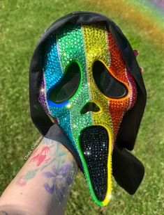 a person wearing a colorful mask on top of their hand in front of a rainbow colored field