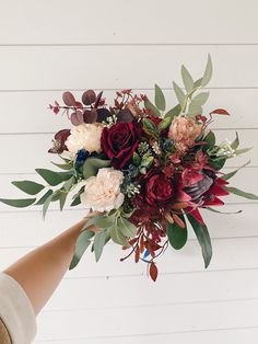 a bouquet of flowers being held by someone's hand on a white wall background