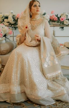 a woman in a white wedding dress sitting on a chair wearing a veil and jewelry