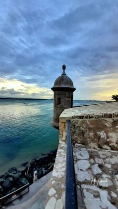 an old tower sitting on top of a stone wall next to the ocean under a cloudy sky