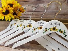 three sunflowers are hanging from hooks on a wooden rack with personalized hangers