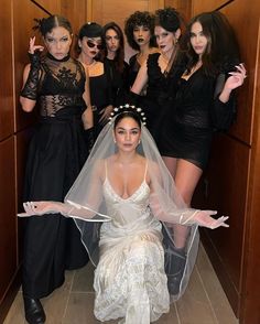 a group of women in black dresses and veils posing for the camera with one woman dressed as a bride