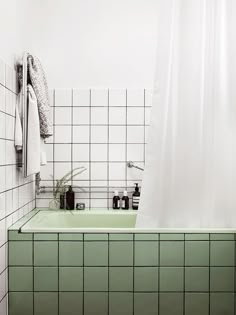 a bathroom with green tiles and white walls, including a bathtub in the corner