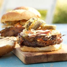 two hamburgers sitting on top of a wooden cutting board