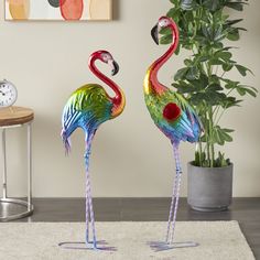 two colorful flamingos standing next to each other in front of a potted plant