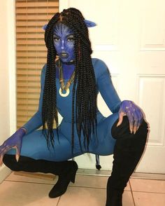 a woman with blue makeup and long braids sitting on the floor in front of a door