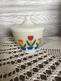 a white bowl with colorful flowers painted on the side sitting on top of a doily