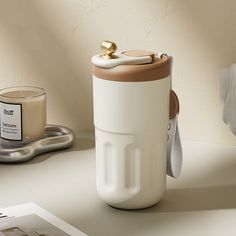 a white and brown coffee cup sitting on top of a table next to a candle