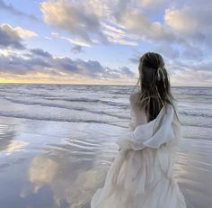 a woman standing on top of a beach next to the ocean under a cloudy sky