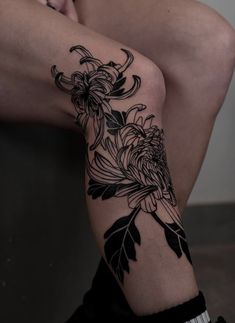 a woman's legs with flowers and leaves tattooed on her leg, sitting in front of a wall