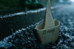 a paper boat sitting on the side of a road next to a street light in the rain