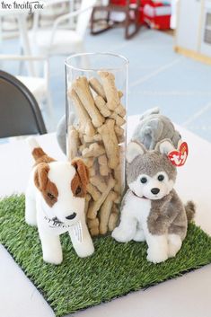 two stuffed dogs sitting next to each other in front of a glass filled with dog treats